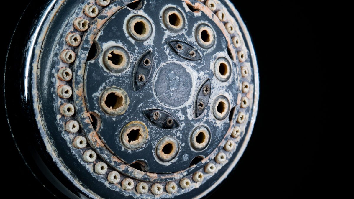 Hard water calcium or lime scale deposits on old, worn out shower head.